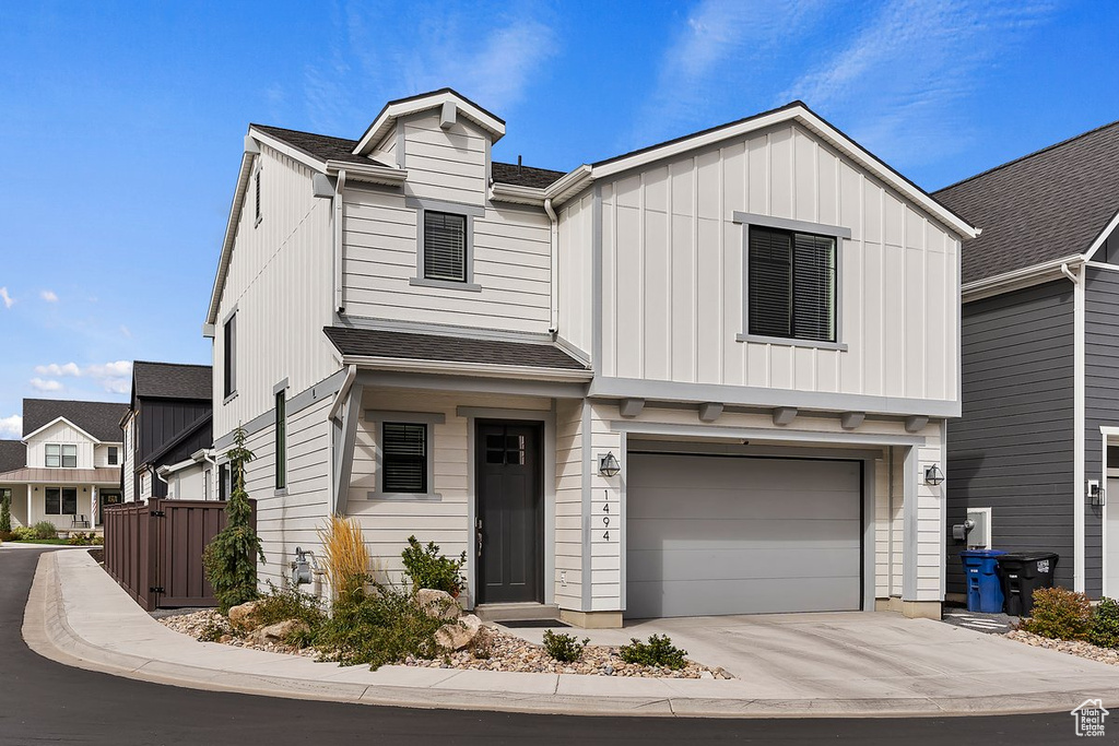 View of front of house featuring an attached garage, concrete driveway, board and batten siding, and roof with shingles