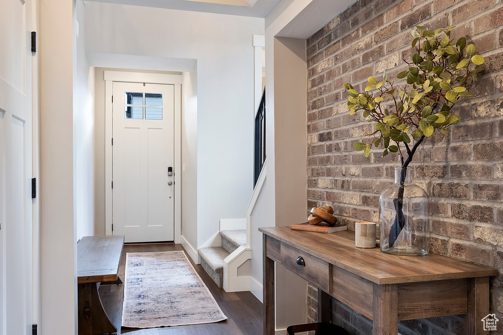 Entrance foyer with brick wall, dark wood finished floors, baseboards, and stairs