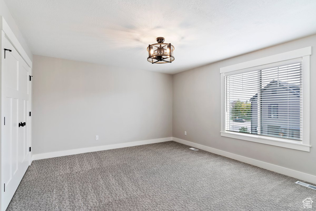 Unfurnished room featuring carpet floors, baseboards, and a chandelier