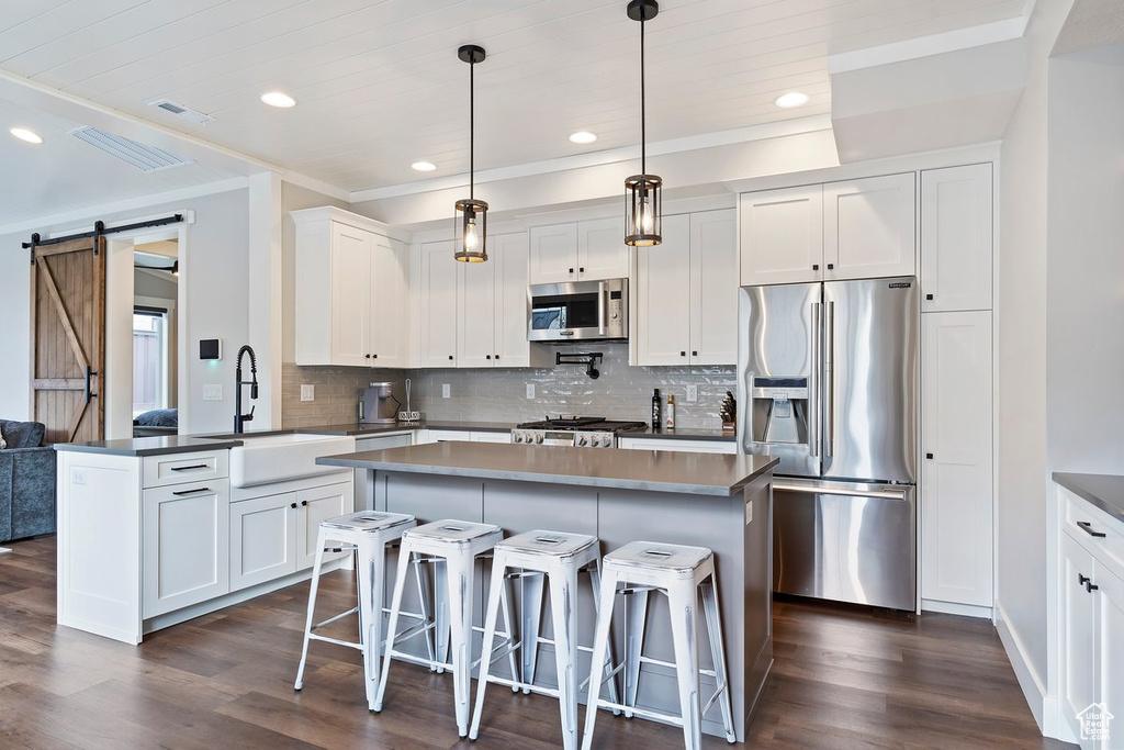 Kitchen featuring appliances with stainless steel finishes, a sink, a barn door, backsplash, and dark wood-type flooring