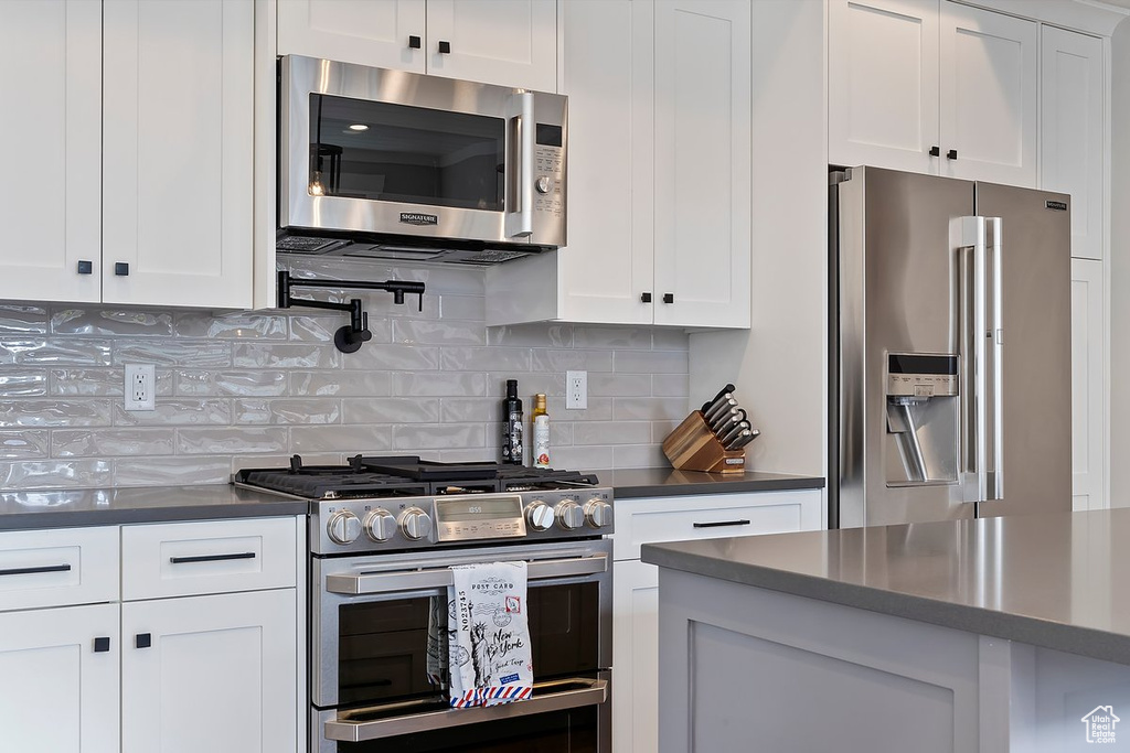 Kitchen featuring stainless steel appliances, dark countertops, white cabinets, and tasteful backsplash