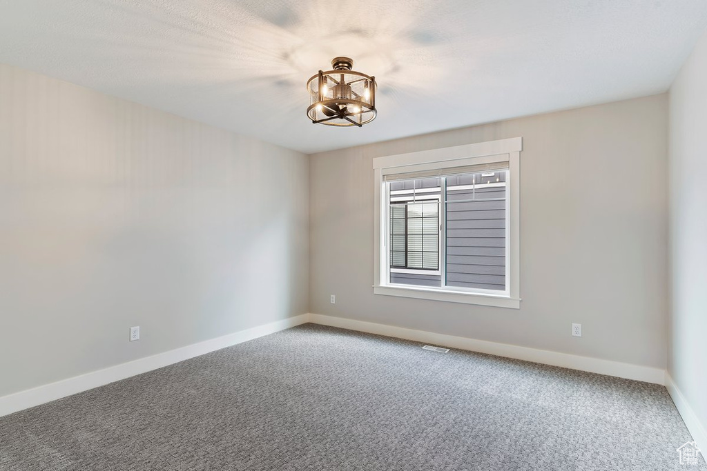 Carpeted empty room featuring a chandelier and baseboards