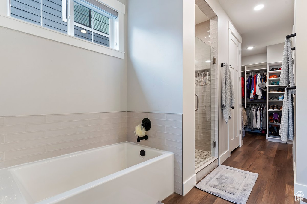Bathroom featuring a bath, a shower stall, a walk in closet, wood finished floors, and recessed lighting