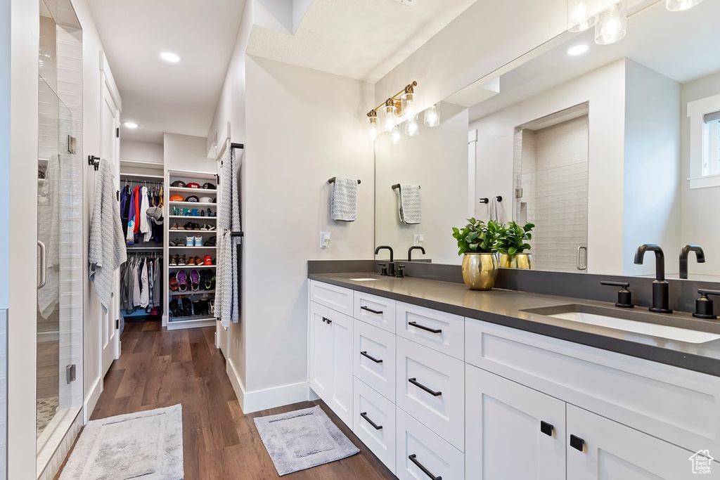 Bathroom with double vanity, a shower stall, a walk in closet, wood finished floors, and baseboards