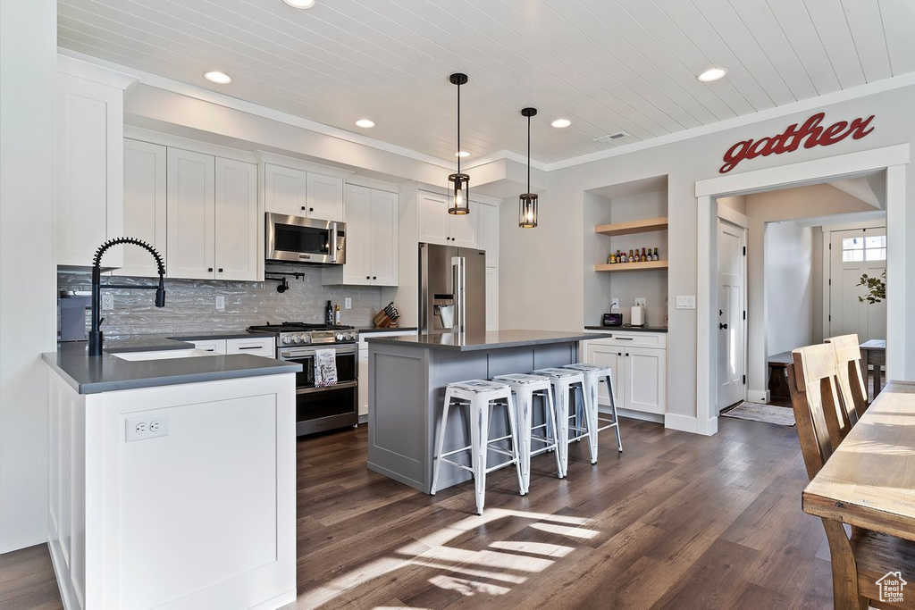Kitchen with appliances with stainless steel finishes, dark countertops, open shelves, white cabinetry, and a sink