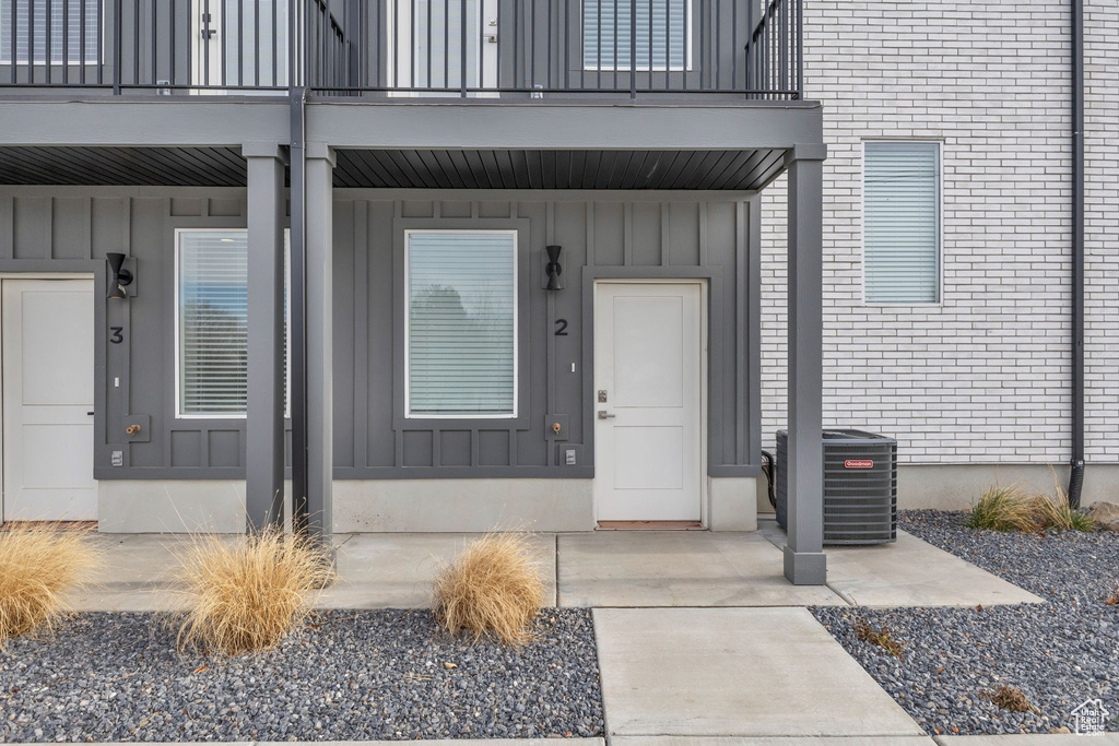 Property entrance with a balcony, board and batten siding, cooling unit, and brick siding
