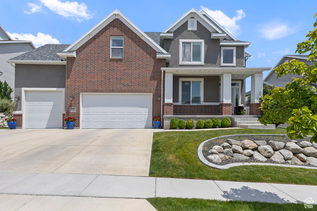 View of front of home featuring stucco siding, covered porch, driveway, a front yard, and brick siding