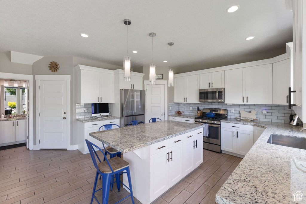 Kitchen featuring appliances with stainless steel finishes, a kitchen island, decorative backsplash, wood tiled floors, and a kitchen bar