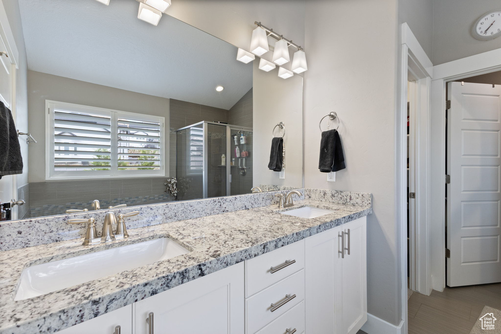 Full bathroom featuring a stall shower, double vanity, and baseboards