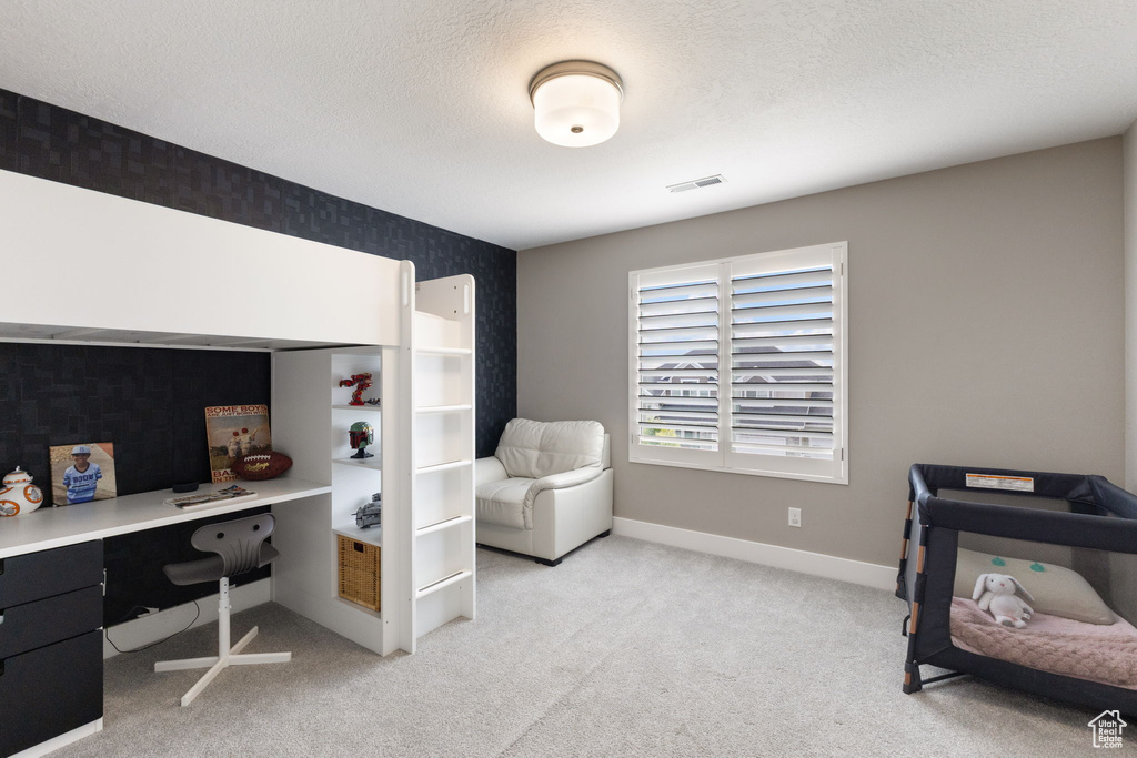 Bedroom featuring wallpapered walls, light colored carpet, baseboards, a desk, and a textured ceiling