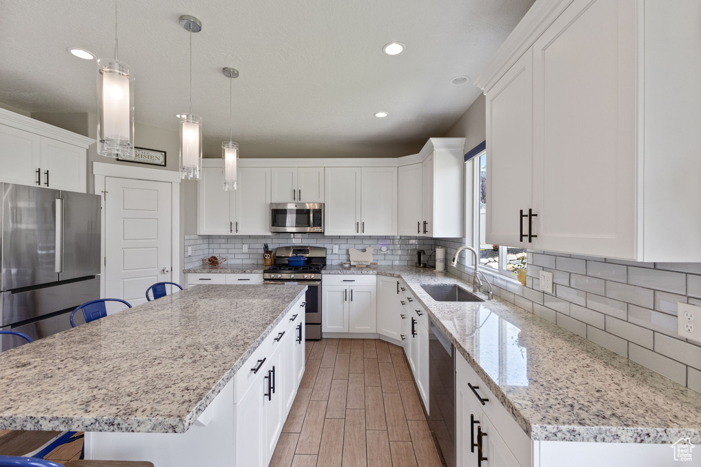 Kitchen with stainless steel appliances, a sink, a kitchen island, backsplash, and white cabinetry