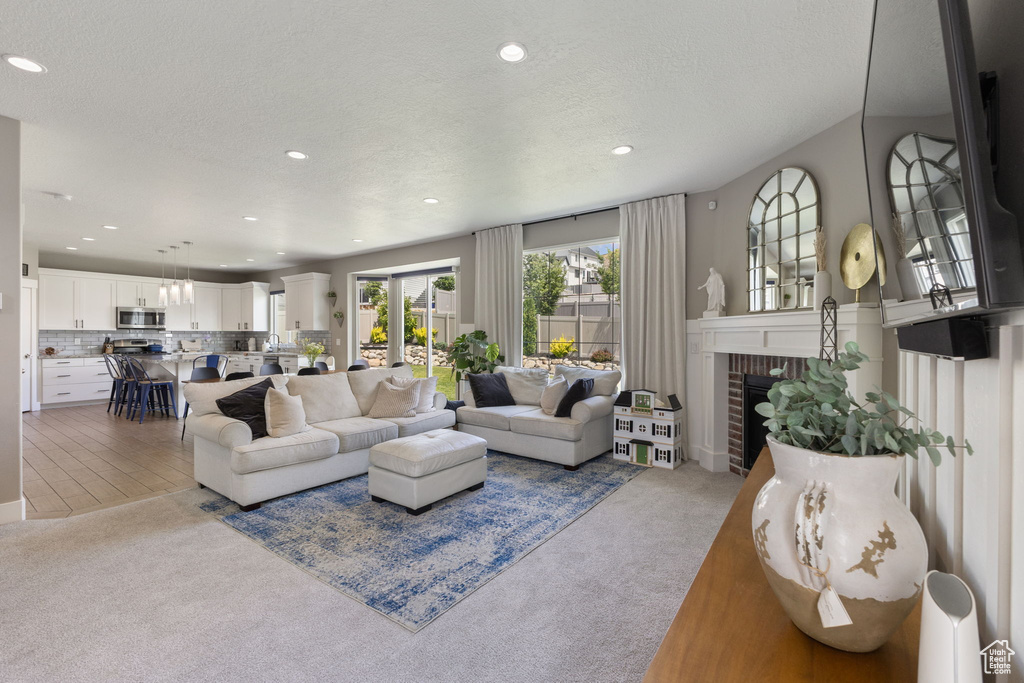 Living area featuring carpet flooring, recessed lighting, a brick fireplace, and a textured ceiling