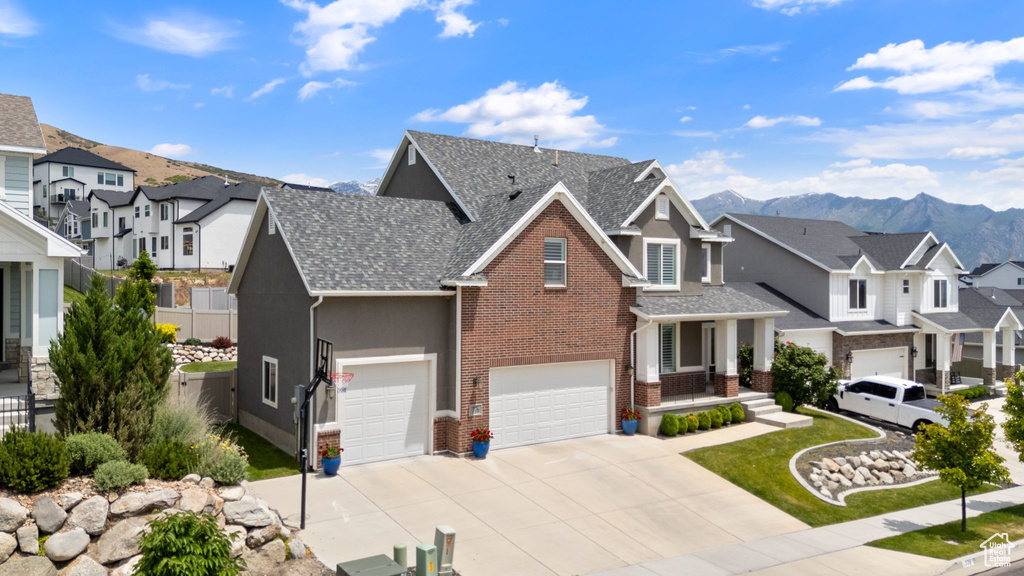 View of front of property with a residential view, driveway, brick siding, a mountain view, and a garage