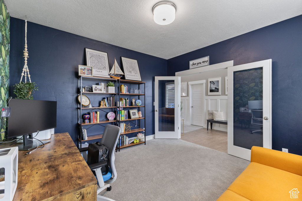 Carpeted office with french doors and a textured ceiling
