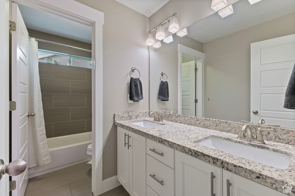 Full bath with double vanity, toilet, shower / bath combination with curtain, and baseboards