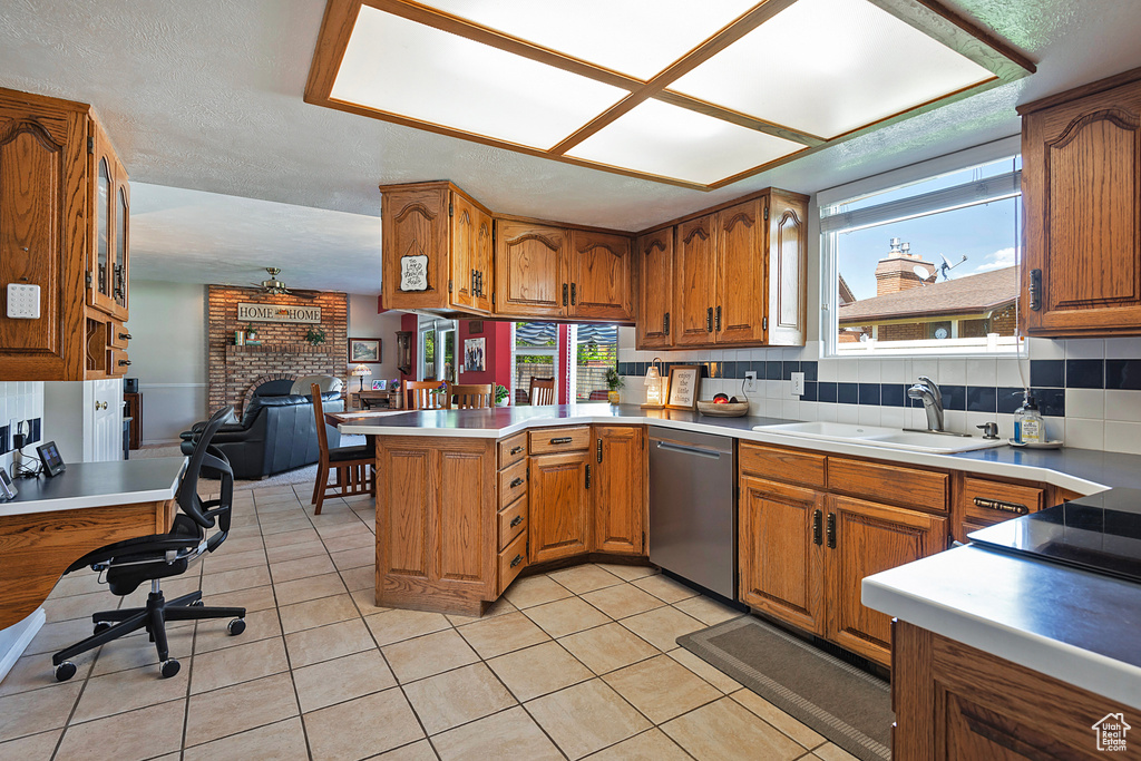 Kitchen featuring dishwasher, a sink, brown cabinetry, a peninsula, and a fireplace
