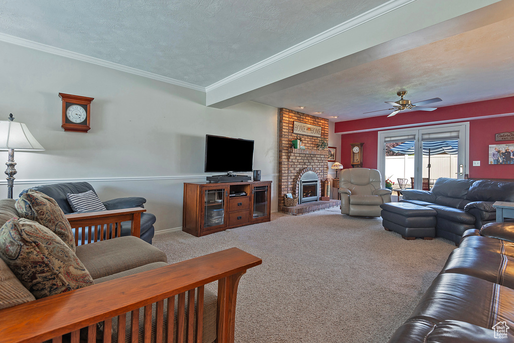 Living area featuring carpet flooring, ceiling fan, ornamental molding, a fireplace, and a textured ceiling