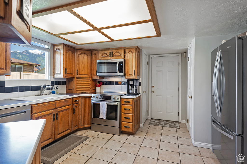 Kitchen featuring stainless steel appliances, brown cabinets, light tile patterned floors, and decorative backsplash