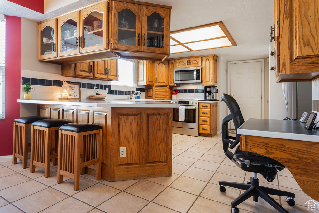Kitchen with appliances with stainless steel finishes, a peninsula, light tile patterned floors, and glass insert cabinets