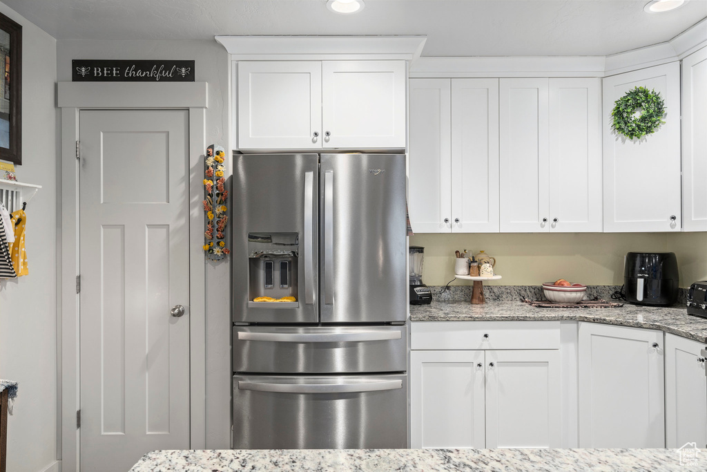 Kitchen featuring stainless steel fridge, white cabinetry, and light stone countertops