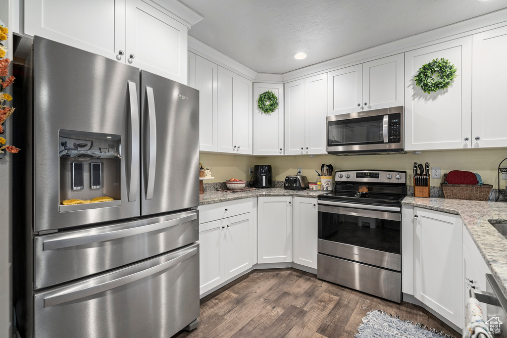 Kitchen with stainless steel appliances, white cabinets, dark wood-style floors, recessed lighting, and light stone counters
