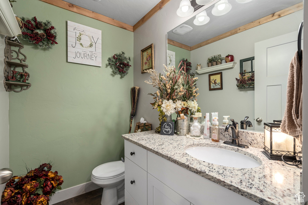 Bathroom featuring toilet, vanity, ornamental molding, wood finished floors, and baseboards