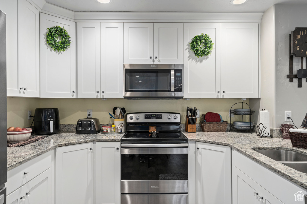 Kitchen with appliances with stainless steel finishes, white cabinets, a sink, light stone counters, and recessed lighting