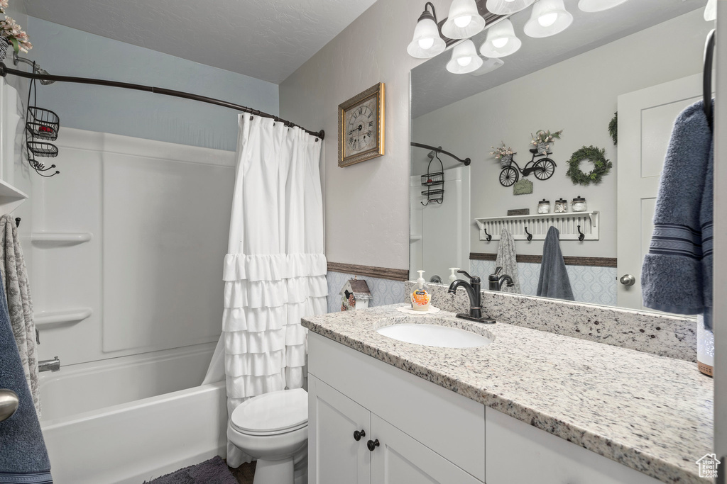 Bathroom with vanity, wainscoting, shower / tub combo, toilet, and a chandelier