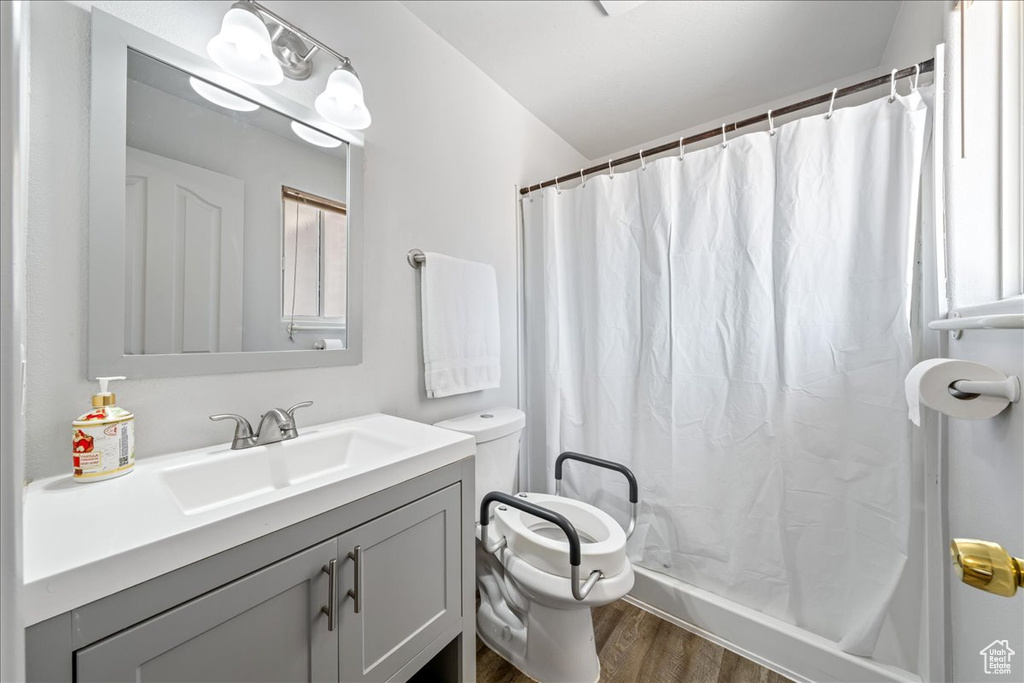 Bathroom with toilet, wood finished floors, vanity, a shower with shower curtain, and vaulted ceiling