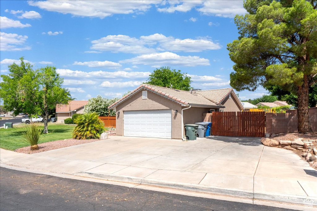 Ranch-style house with a tile roof, stucco siding, concrete driveway, an attached garage, and a gate