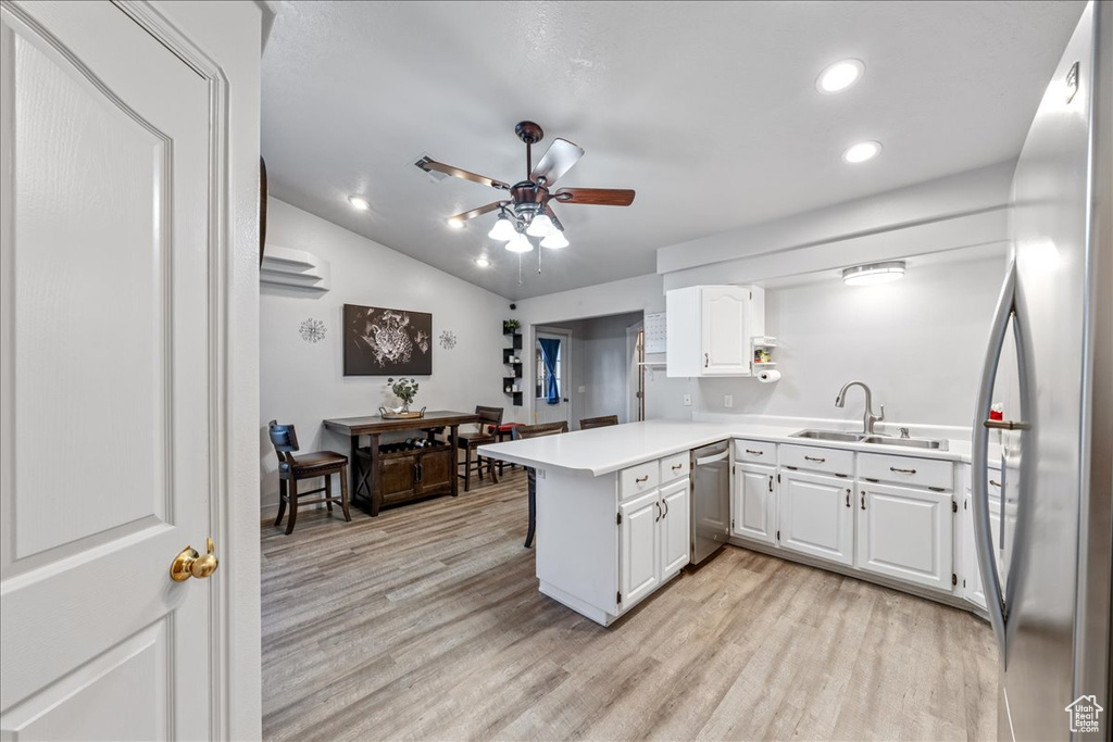 Kitchen featuring appliances with stainless steel finishes, a sink, a peninsula, light countertops, and white cabinetry