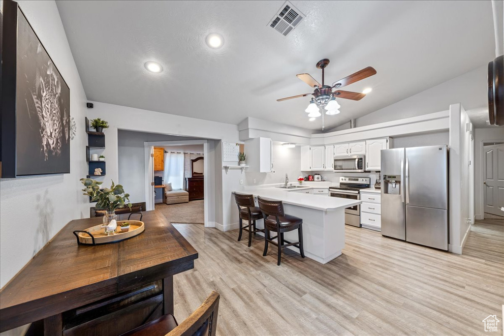 Kitchen featuring appliances with stainless steel finishes, a peninsula, light countertops, a ceiling fan, and vaulted ceiling