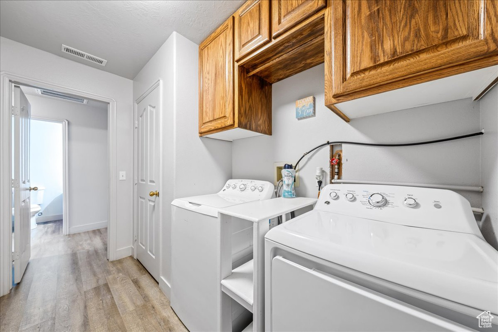 Laundry area featuring cabinet space, washing machine and dryer, light wood-style floors, and baseboards