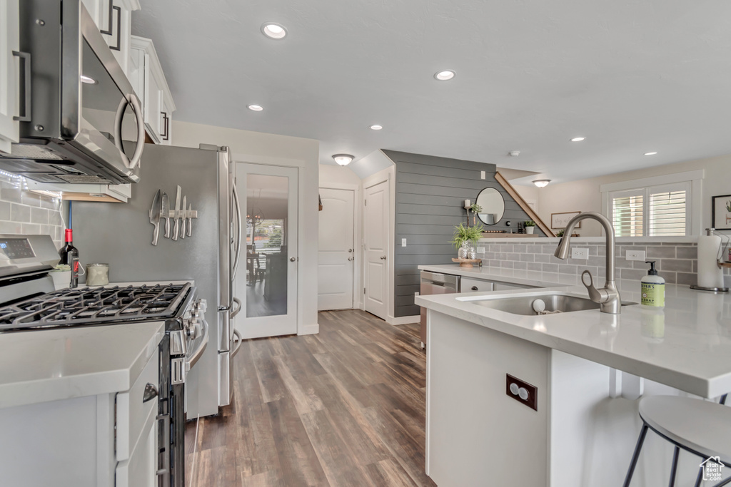 Kitchen with stainless steel appliances, a sink, backsplash, a kitchen breakfast bar, and recessed lighting