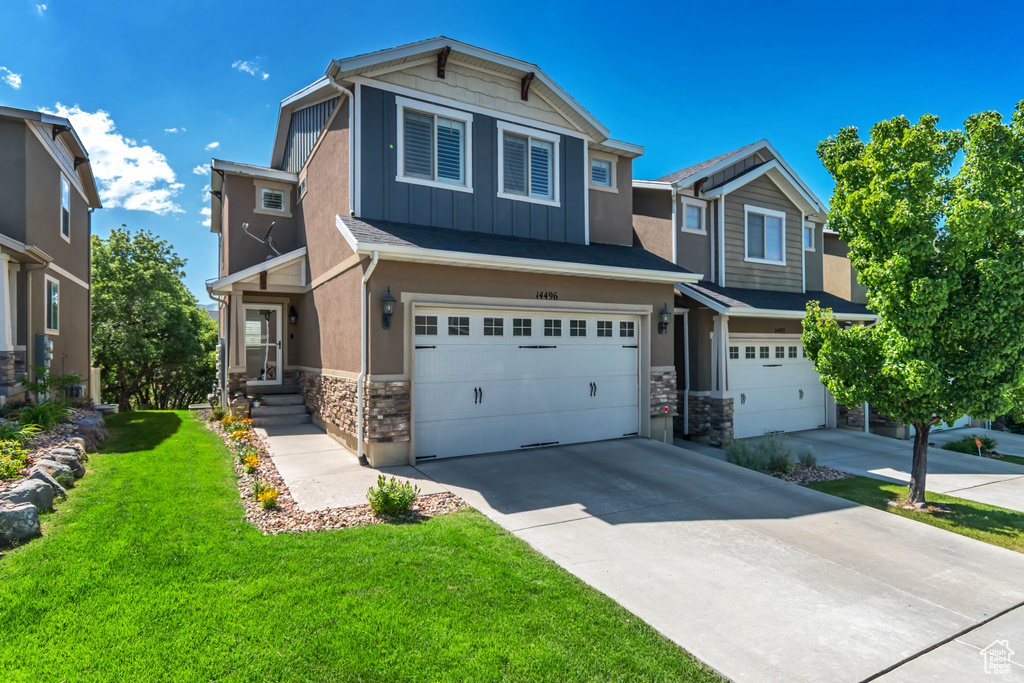 Craftsman-style home with stone siding, a garage, board and batten siding, concrete driveway, and a front lawn