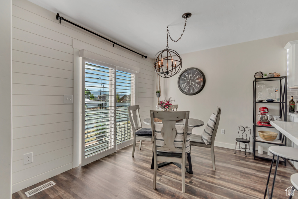 Dining area with a chandelier, dark wood finished floors, wood walls, and baseboards