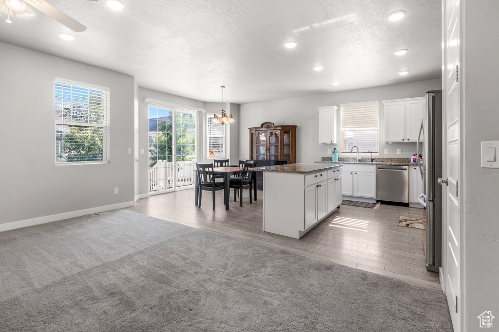 Kitchen featuring stainless steel appliances, a chandelier, baseboards, a kitchen island, and light colored carpet
