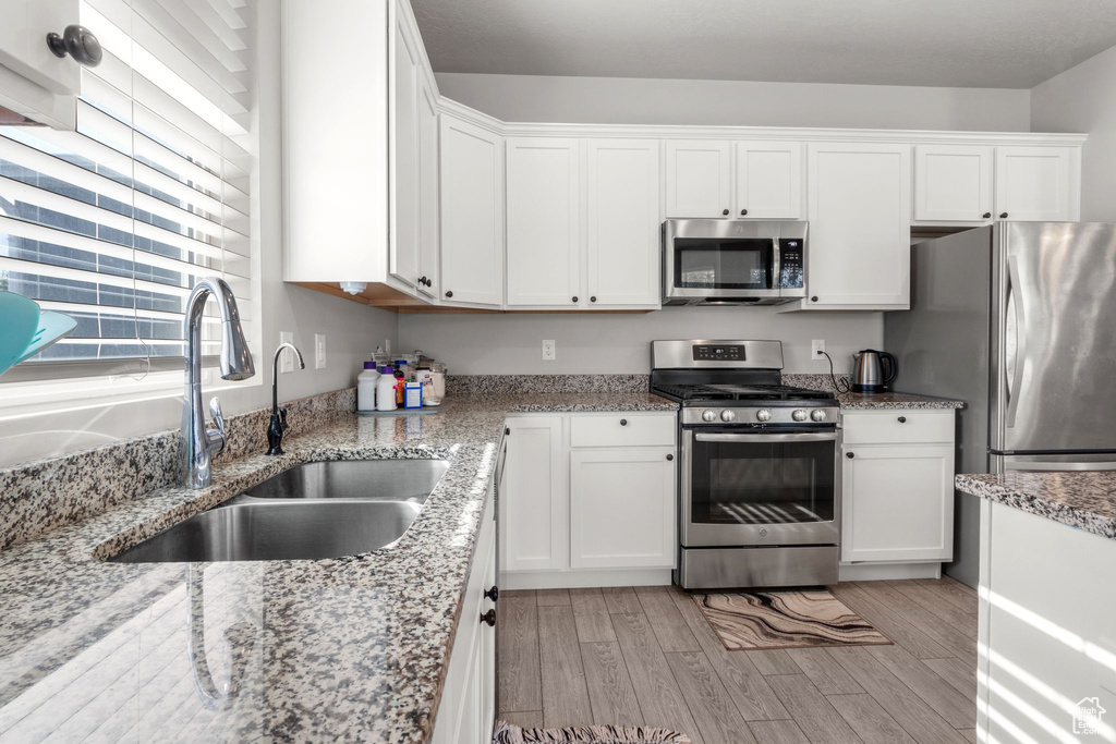 Kitchen with appliances with stainless steel finishes, a sink, white cabinetry, and light wood-type flooring