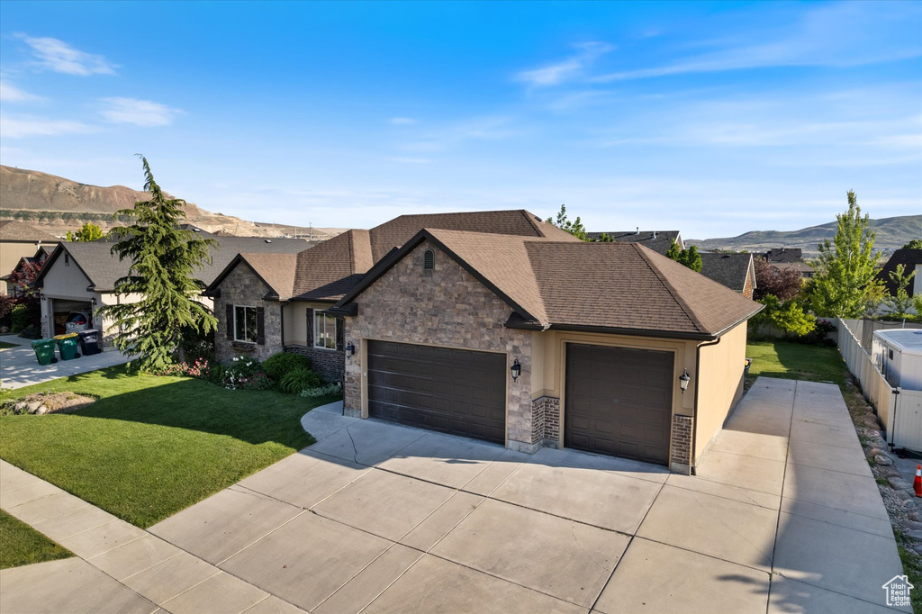View of front of home with an attached garage, driveway, a mountain view, stone siding, and roof with shingles