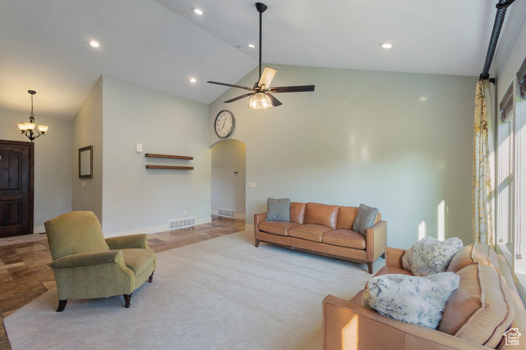 Living room featuring vaulted ceiling, arched walkways, ceiling fan, baseboards, and a chandelier
