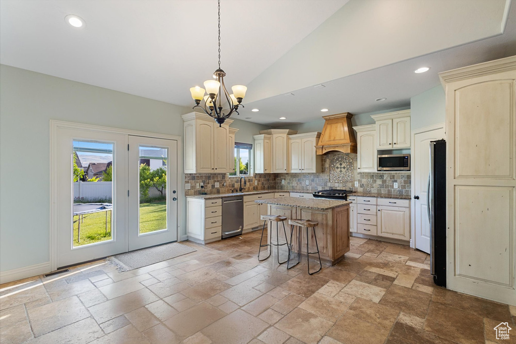 Kitchen featuring cream cabinetry, appliances with stainless steel finishes, custom range hood, a chandelier, and decorative backsplash