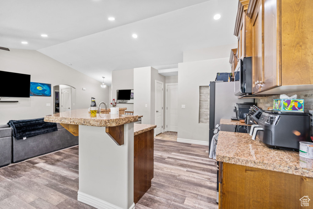 Kitchen featuring open floor plan, light wood-style flooring, stove, a breakfast bar area, and vaulted ceiling