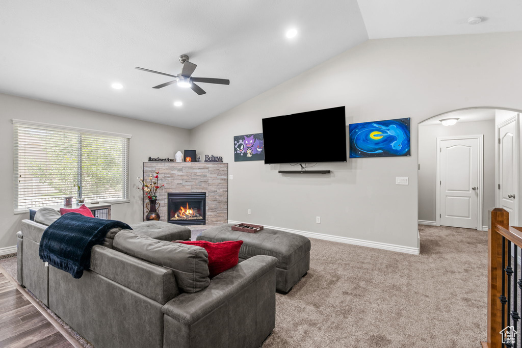 Carpeted living room featuring lofted ceiling, ceiling fan, baseboards, a stone fireplace, and arched walkways