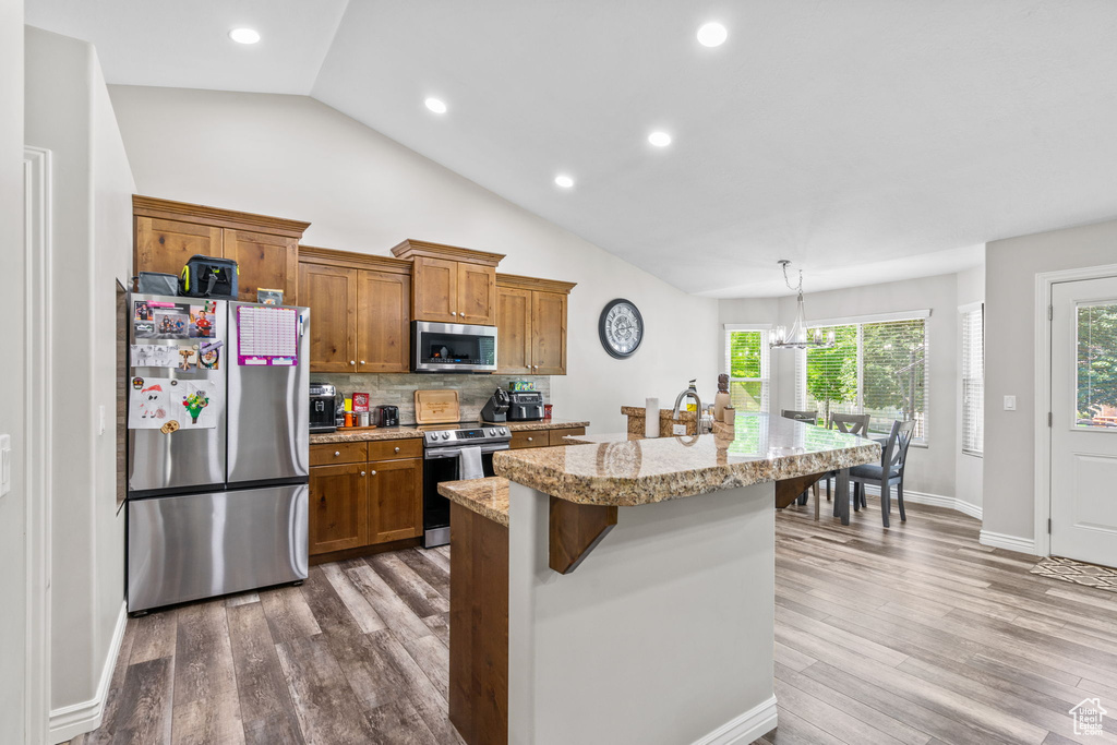 Kitchen with stainless steel appliances, brown cabinets, a kitchen island, backsplash, and vaulted ceiling