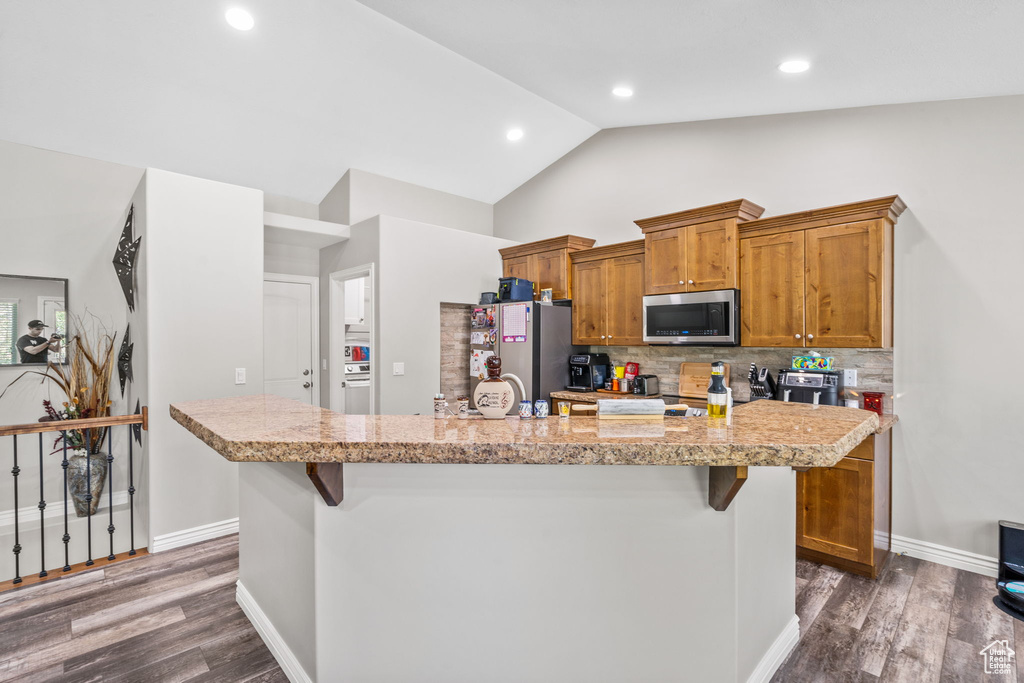 Kitchen featuring stainless steel appliances, a kitchen breakfast bar, light countertops, decorative backsplash, and lofted ceiling