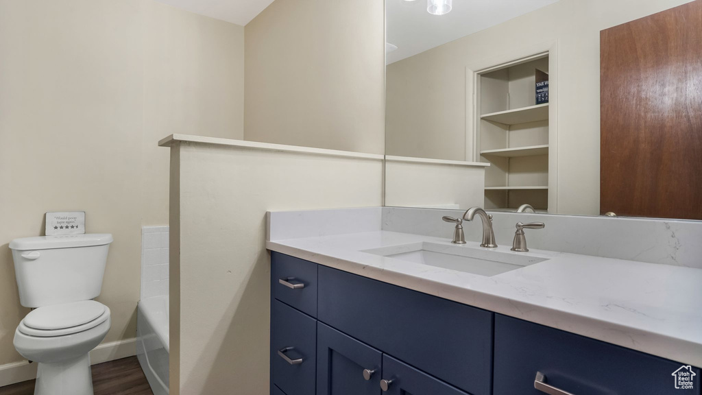 Bathroom featuring toilet, vanity, a tub, wood finished floors, and baseboards