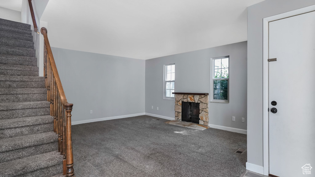 Unfurnished living room featuring stairway, baseboards, and dark carpet