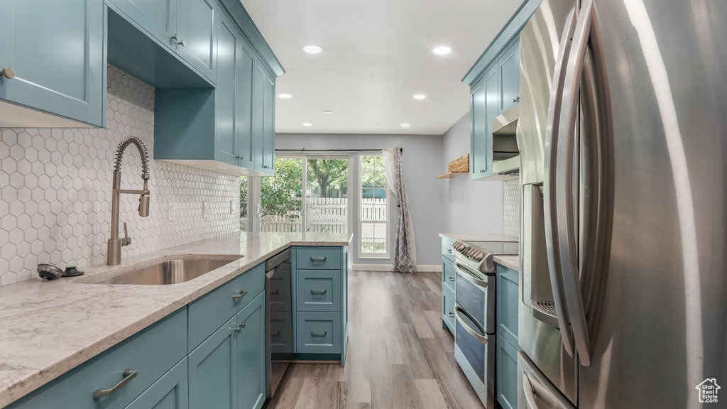 Kitchen with stainless steel appliances, a sink, wood finished floors, backsplash, and recessed lighting