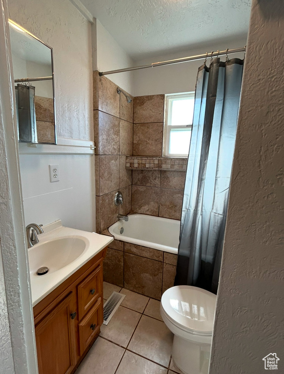 Bathroom with a textured ceiling, tiled shower / bath combo, tile patterned floors, vanity, and a textured wall