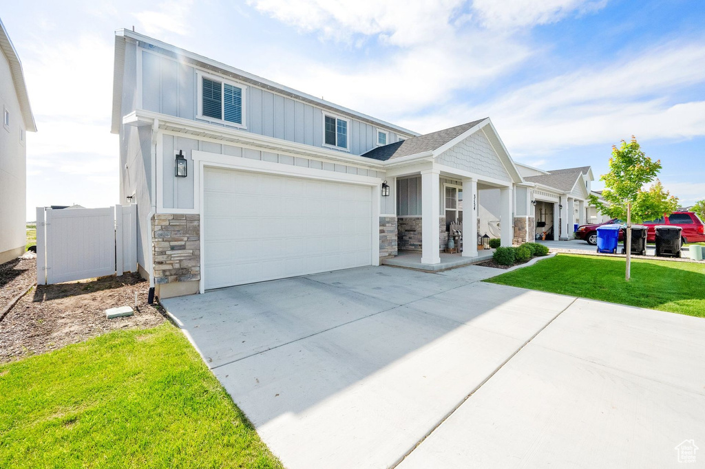 View of front of house featuring stone siding, board and batten siding, concrete driveway, and a front lawn